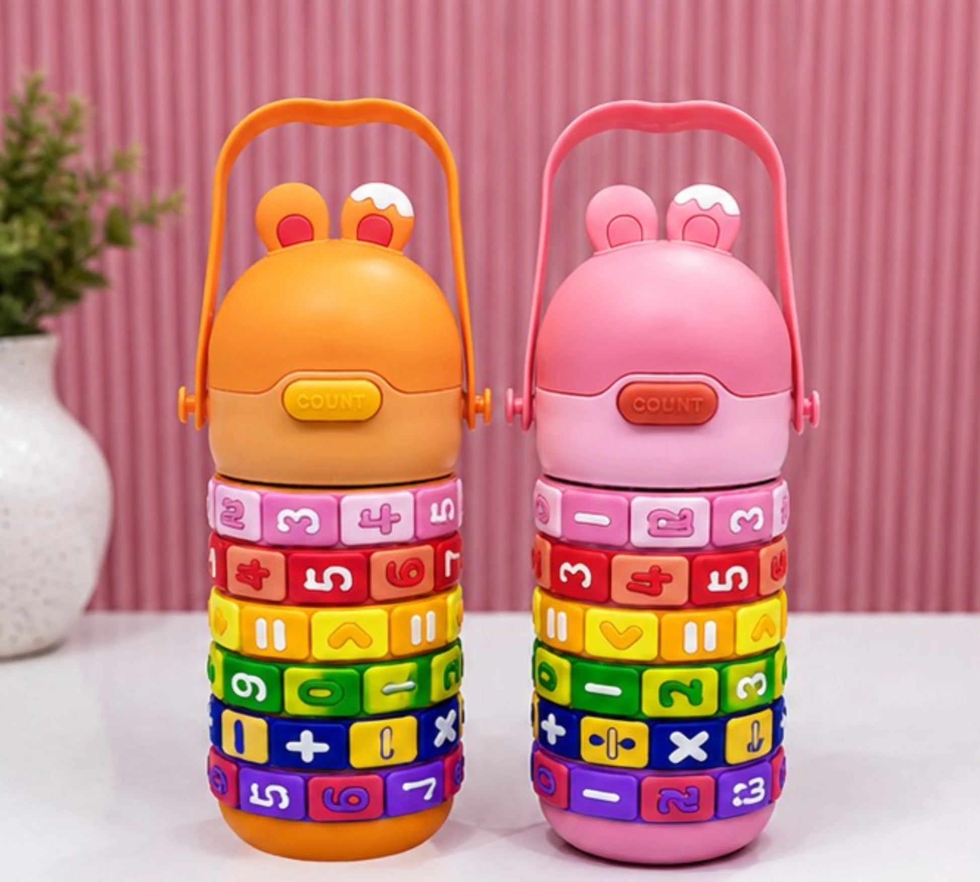 Two colorful children's stackable toys with number and letter patterns on a pink background.